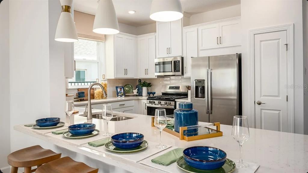 A modern kitchen features white cabinets, stainless steel appliances, and a large quartz-topped island — 11291 SILVER TRUMPET LOOP, WINTER GARDEN, FL