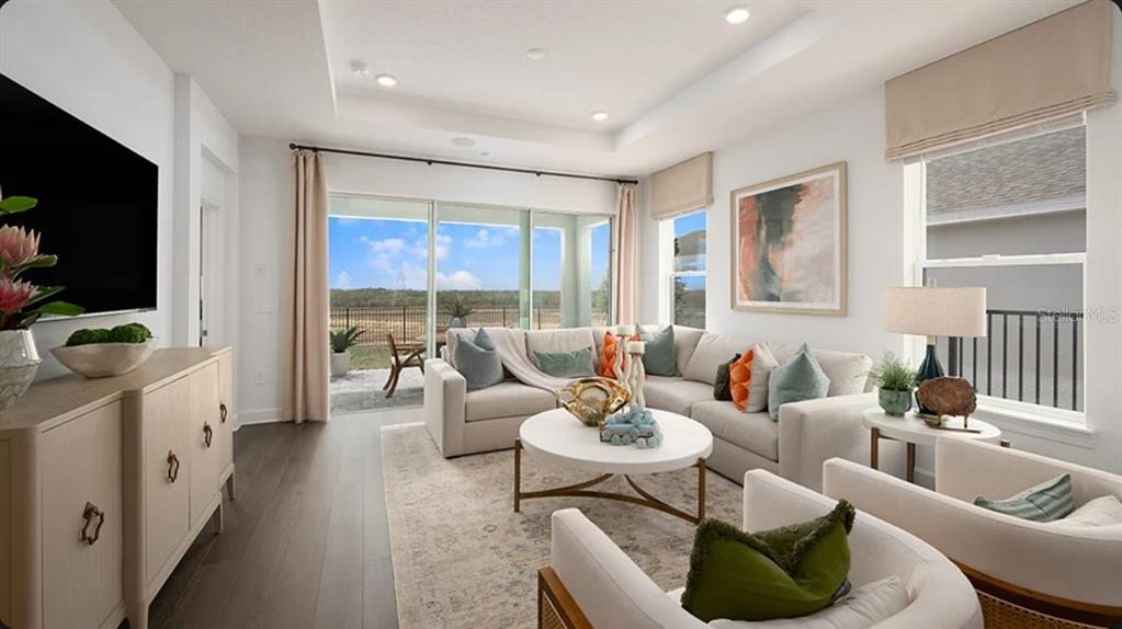 A bright living room features a sectional sofa, white armchairs, and sliding glass doors — 11291 SILVER TRUMPET LOOP, WINTER GARDEN, FL
