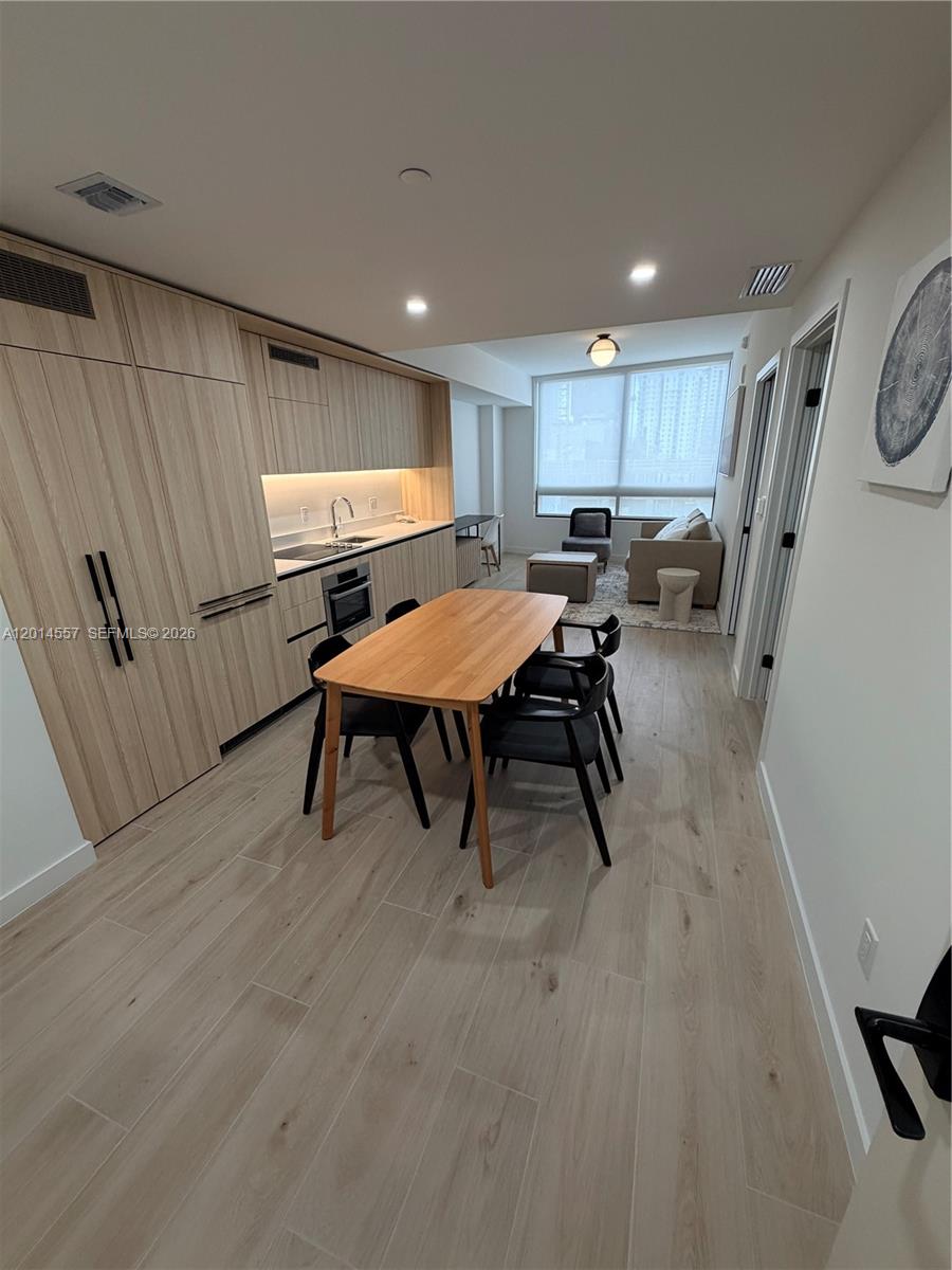 This open-concept kitchen and dining area features light wood cabinetry and matching flooring — 225 N Miami av # 907, Miami FL 33128, MIAMI, FL