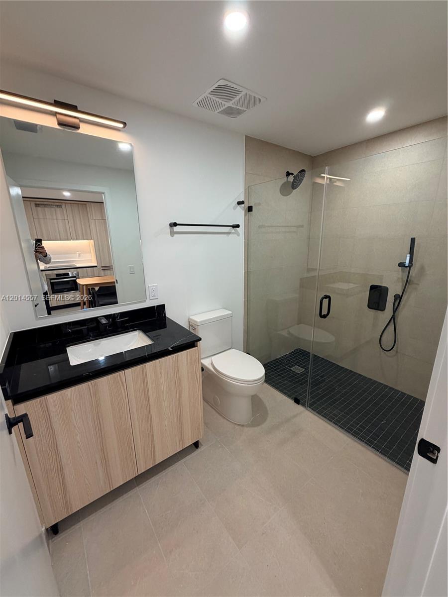 A modern bathroom features a wood vanity, black countertop, toilet, and a glass-enclosed walk-in shower — 225 N Miami av # 907, Miami FL 33128, MIAMI, FL