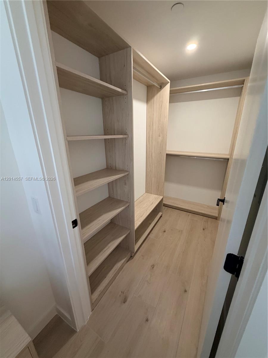 A walk-in closet features light wood-toned shelving and flooring with white walls — 225 N Miami av # 907, Miami FL 33128, MIAMI, FL