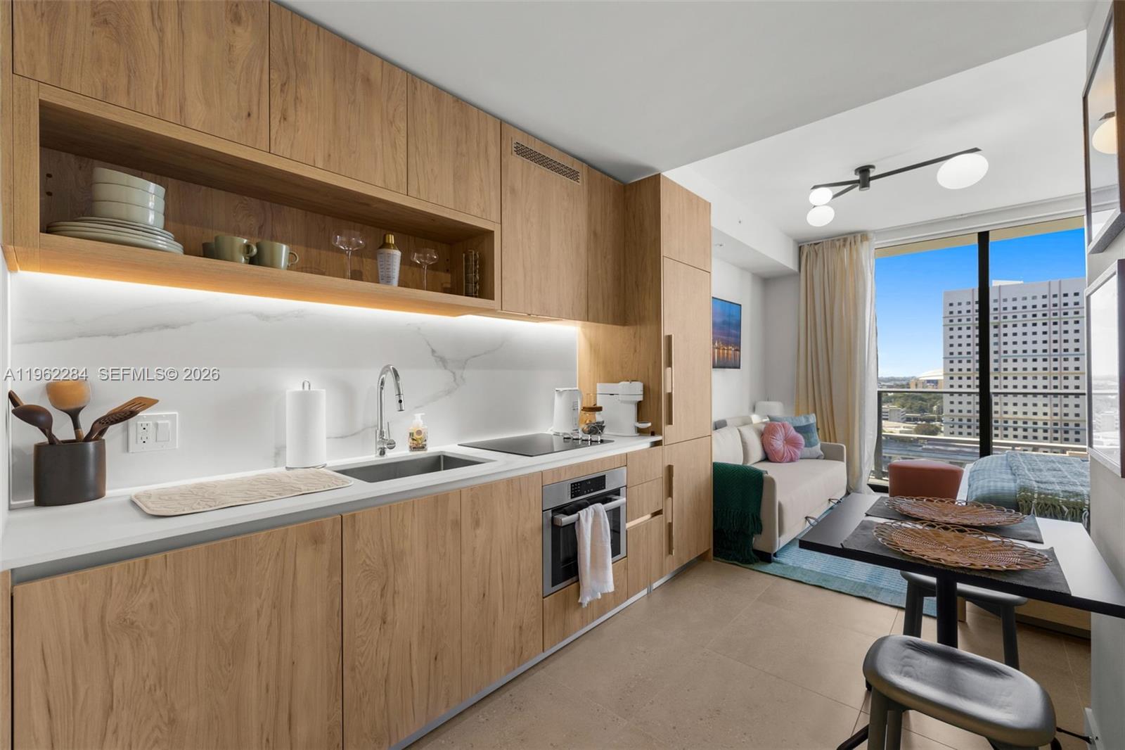 A modern kitchen features light wood cabinetry, white marble-look backsplash, and an adjacent living area — 11 NE 6th St # 1615, Miami FL 33132, MIAMI, FL