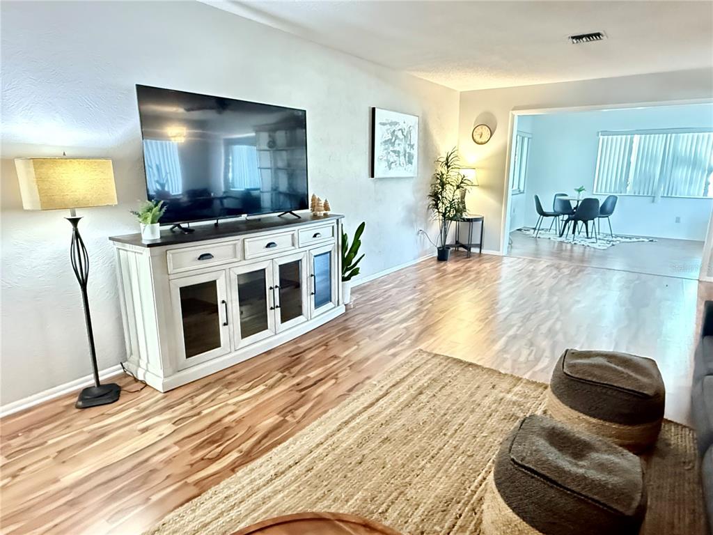 A living room features a large television on a white console, wood-look flooring, and a rug — 709 HICKORY LANE, BRADENTON, FL