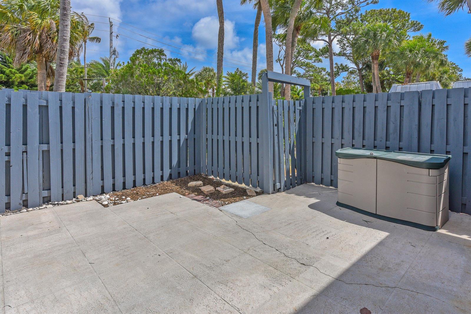 A concrete patio is enclosed by a gray wooden fence with a gate and storage bin — 3802 SE Jefferson Street, Stuart FL 34997, STUART, FL