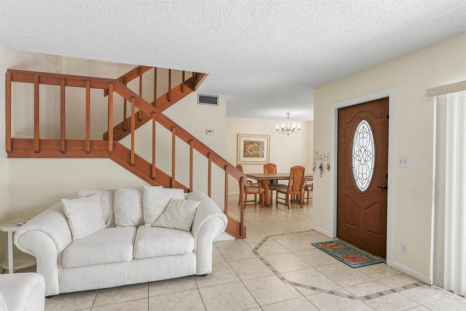A living room features a white sofa, wooden staircase, tiled floors, and a front door — 3802 SE Jefferson Street, Stuart FL 34997, STUART, FL