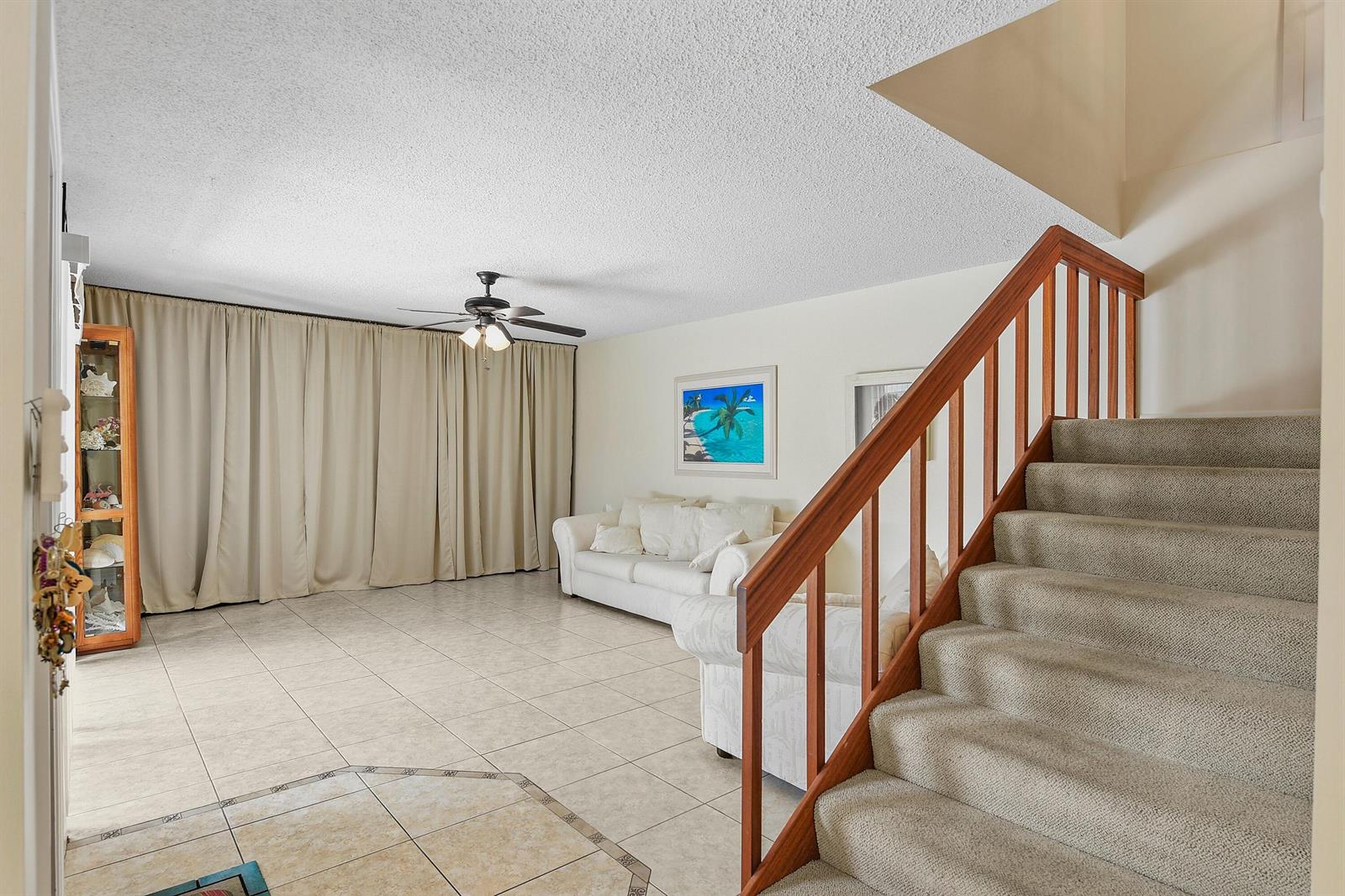 A living room features tile flooring, a carpeted staircase, beige curtains, and a ceiling fan — 3802 SE Jefferson Street, Stuart FL 34997, STUART, FL