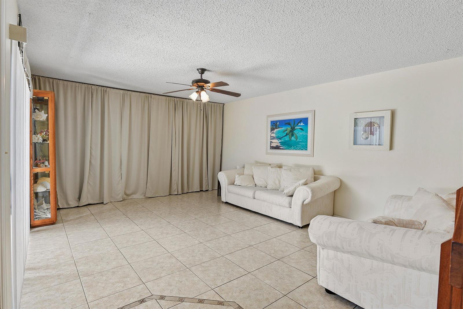 A living room features beige tile floors, a white sofa, and floor-to-ceiling curtains — 3802 SE Jefferson Street, Stuart FL 34997, STUART, FL