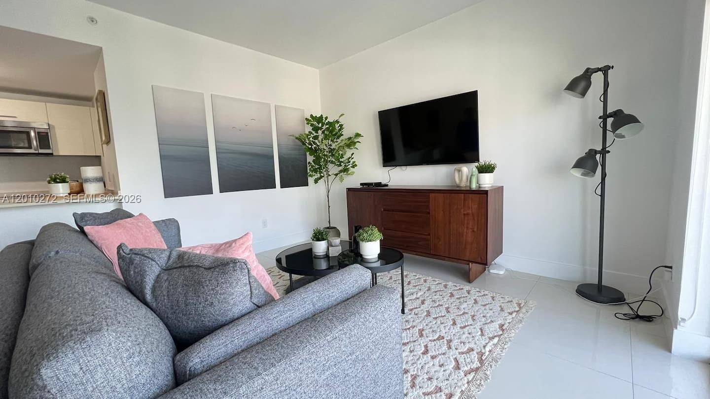 A living room features a grey sofa, a wooden media console, and a floor lamp — 1300 Brickell Bay Dr # 3400, Miami FL 33131, MIAMI, FL