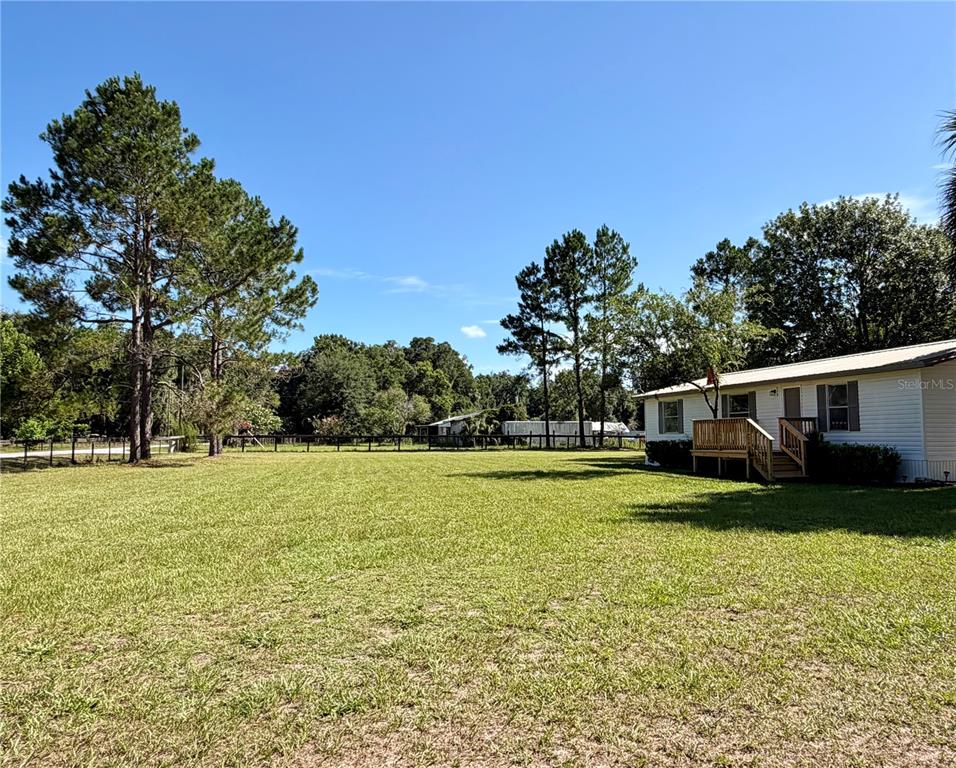 A large grassy yard sits in front of a white house with a wooden deck — 17545 NE 37TH COURT, CITRA, FL