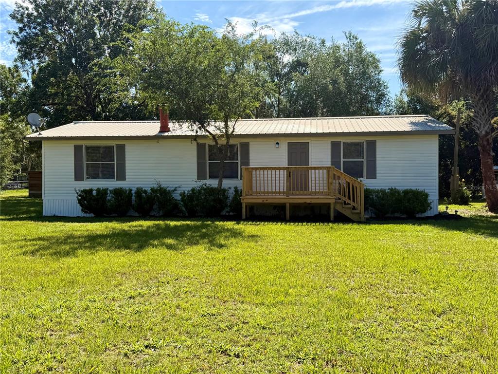 A single-story white house with a metal roof and a wooden front deck — 17545 NE 37TH COURT, CITRA, FL