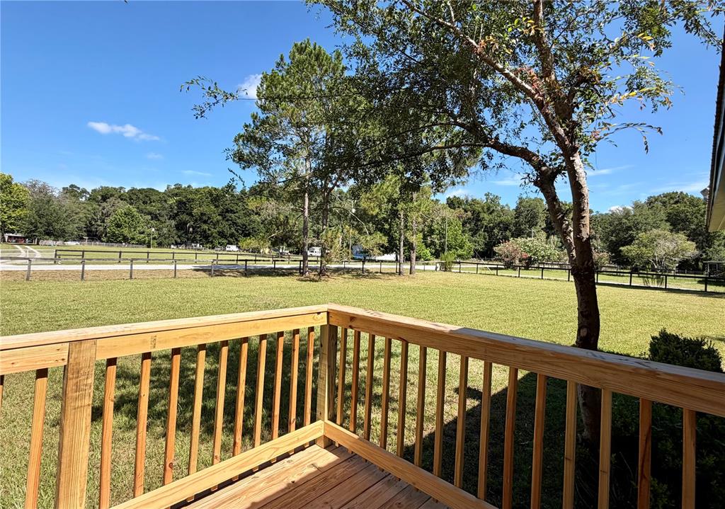A wooden deck with railings overlooks a large grassy yard and a fenced pasture — 17545 NE 37TH COURT, CITRA, FL