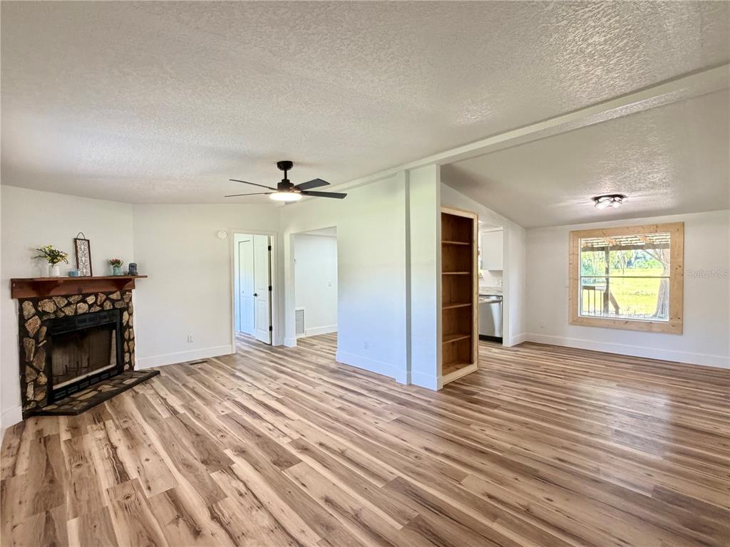 A living room with wood-look flooring, a stone fireplace, and an open kitchen area — 17545 NE 37TH COURT, CITRA, FL