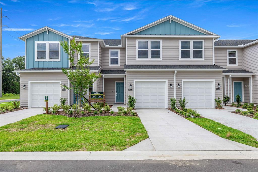 A multi-unit residential building with light gray siding, blue accents, and three attached garages — 4969 SW 83RD PLACE, OCALA, FL