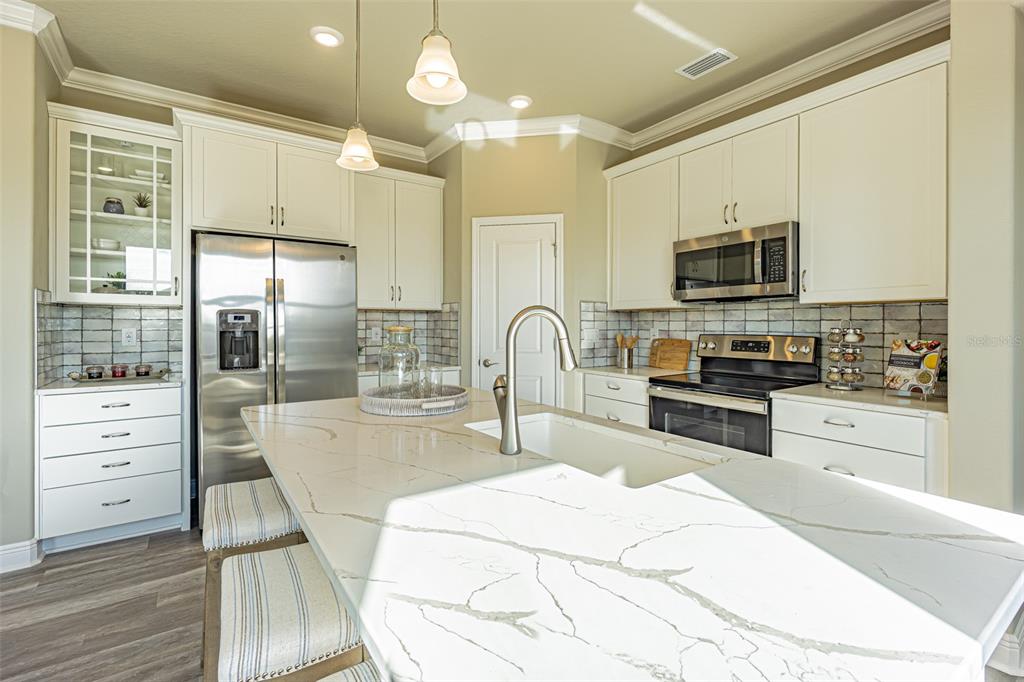 A modern kitchen features white cabinetry, stainless steel appliances, and a large marble-topped island — 9429 HIGHLAND HILLS DRIVE, HUDSON, FL