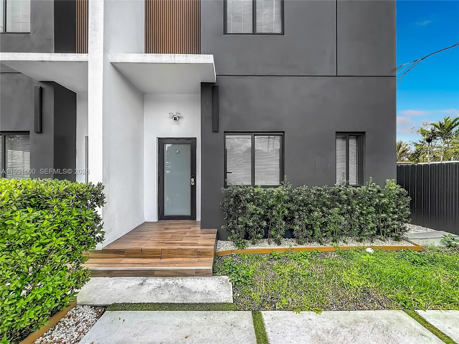 A modern two-story townhouse exterior features a wood-tiled porch, dark gray walls, and landscaping — 1220 & 1222 NW 30th St, Miami FL 33142, MIAMI, FL