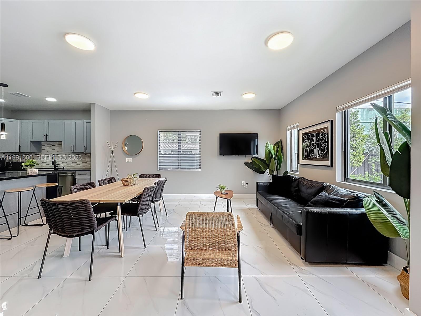 An open-concept living and dining area features white tile floors, a black sofa, and kitchen — 1220 & 1222 NW 30th St, Miami FL 33142, MIAMI, FL