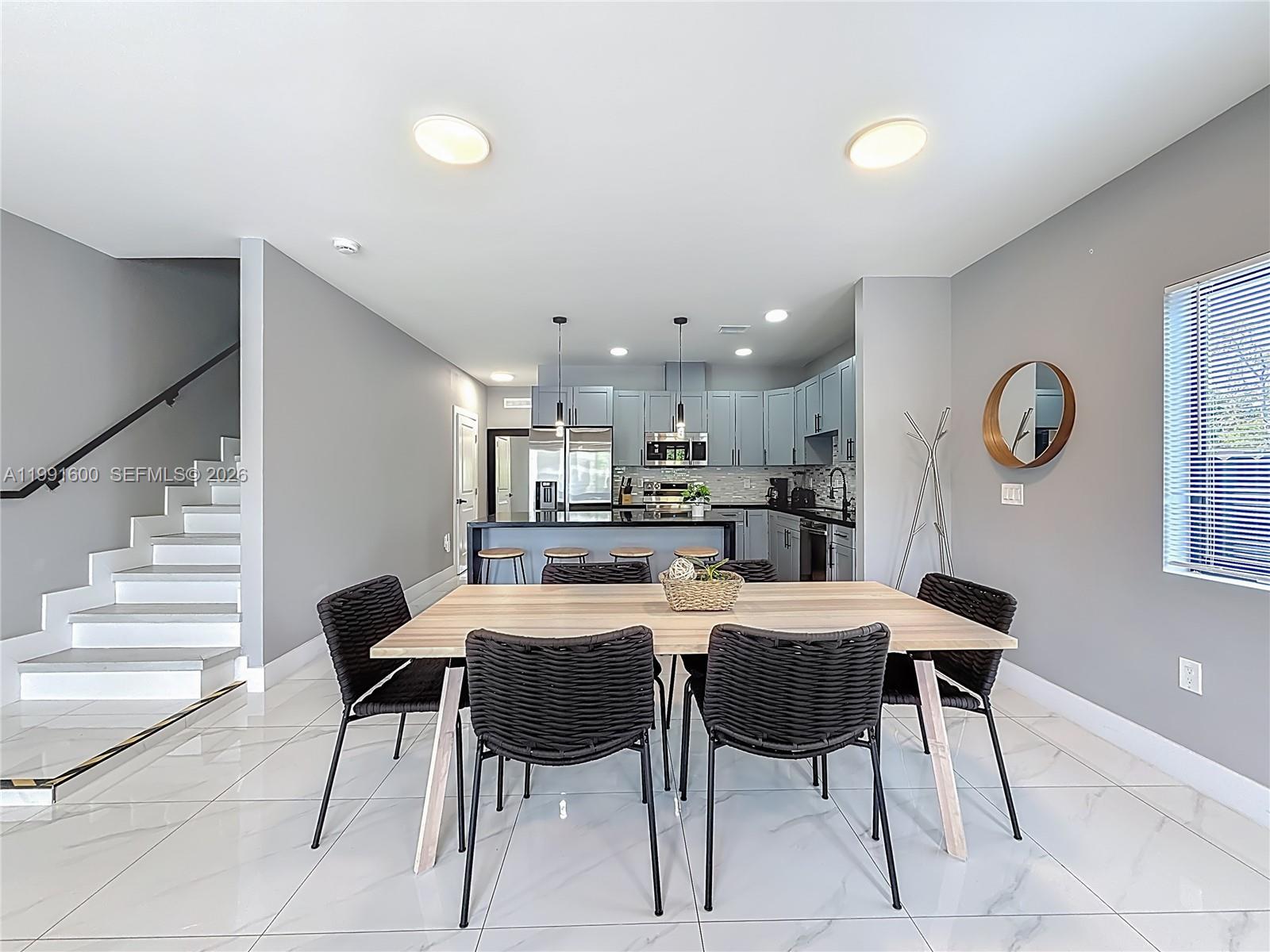 A dining area with a wooden table and black chairs sits before an open kitchen — 1220 & 1222 NW 30th St, Miami FL 33142, MIAMI, FL