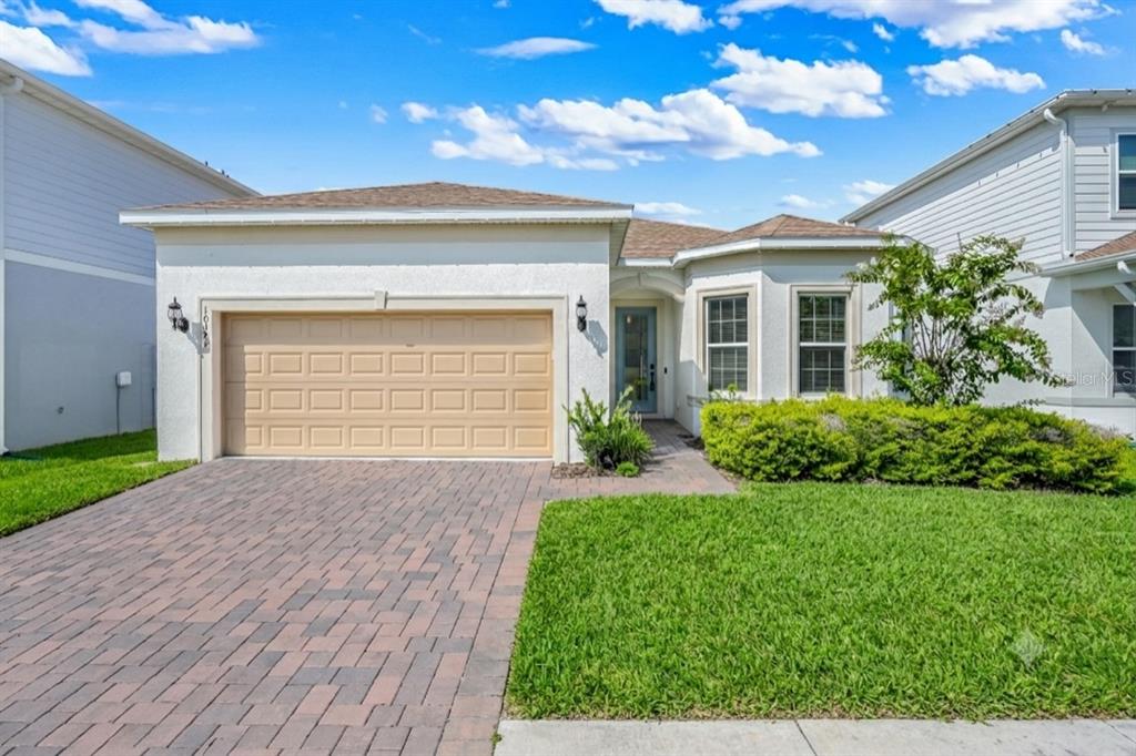 A single-story house with a tan garage, brick paver driveway, and a small front lawn — 10393 PARK ESTATES AVENUE, ORLANDO, FL