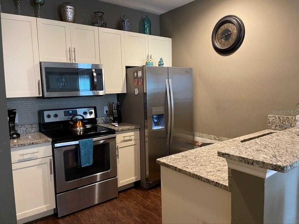 A kitchen features white cabinets, stainless steel appliances, granite countertops, and a dark wall clock — 9004 SHINE DRIVE, KISSIMMEE, FL