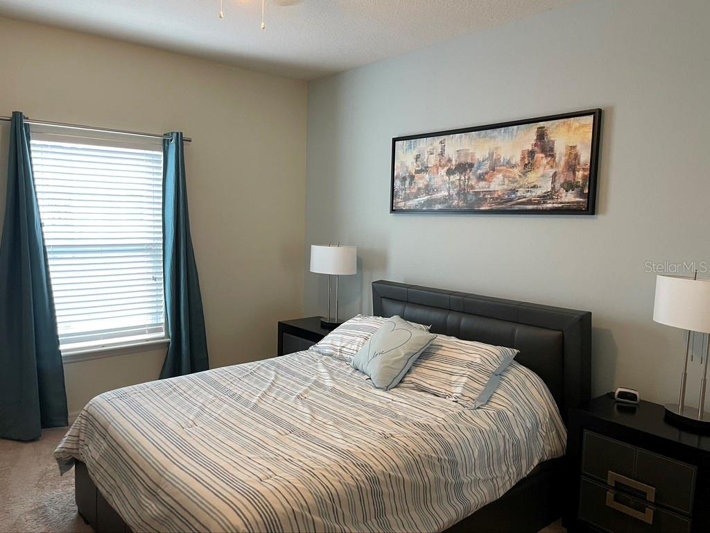 A bedroom features a bed with striped bedding, two nightstands with lamps, and wall art — 9004 SHINE DRIVE, KISSIMMEE, FL