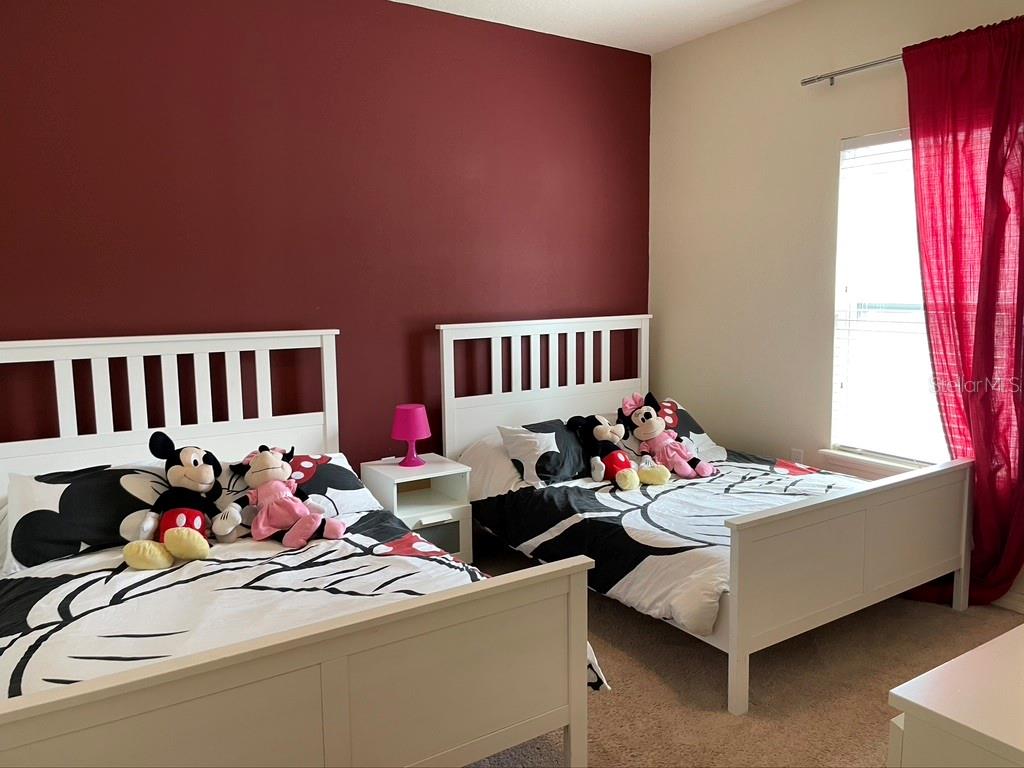 A bedroom features two white beds with Disney-themed bedding against a dark red accent wall — 9004 SHINE DRIVE, KISSIMMEE, FL