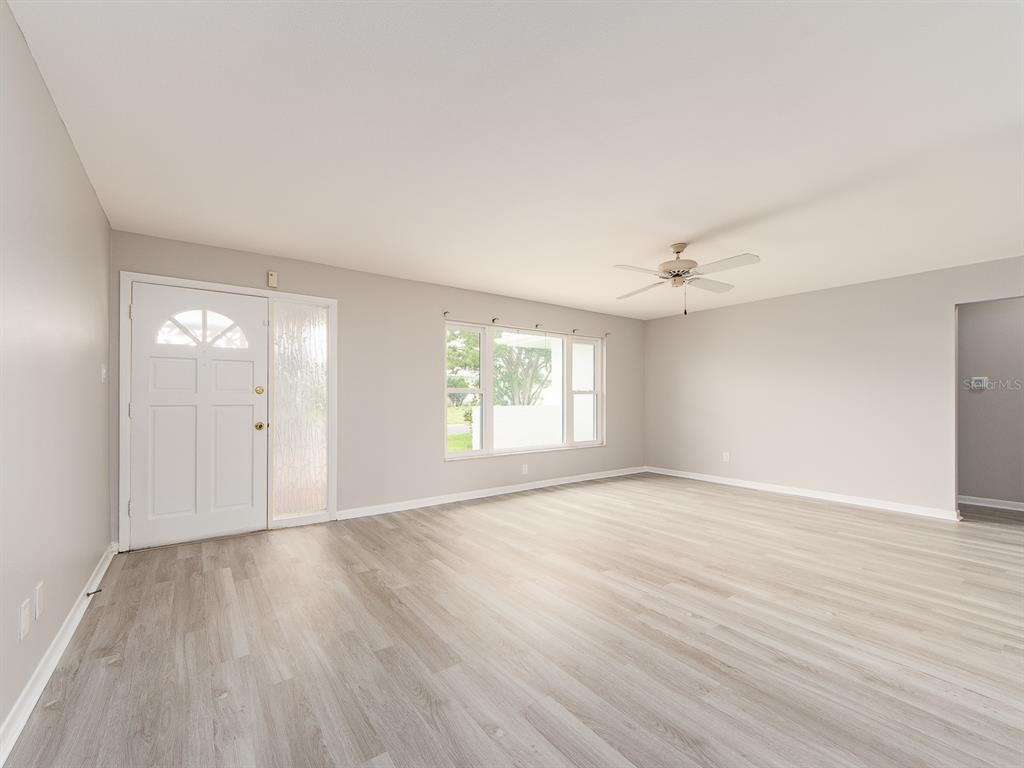 A bright living room features light gray walls, wood-look flooring, a ceiling fan, and windows — 14070 90TH AVENUE, SEMINOLE, FL