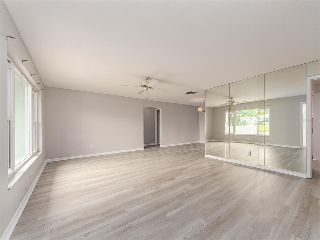 A spacious, empty room features light gray wood-look flooring, neutral walls, and a mirrored wall — 14070 90TH AVENUE, SEMINOLE, FL