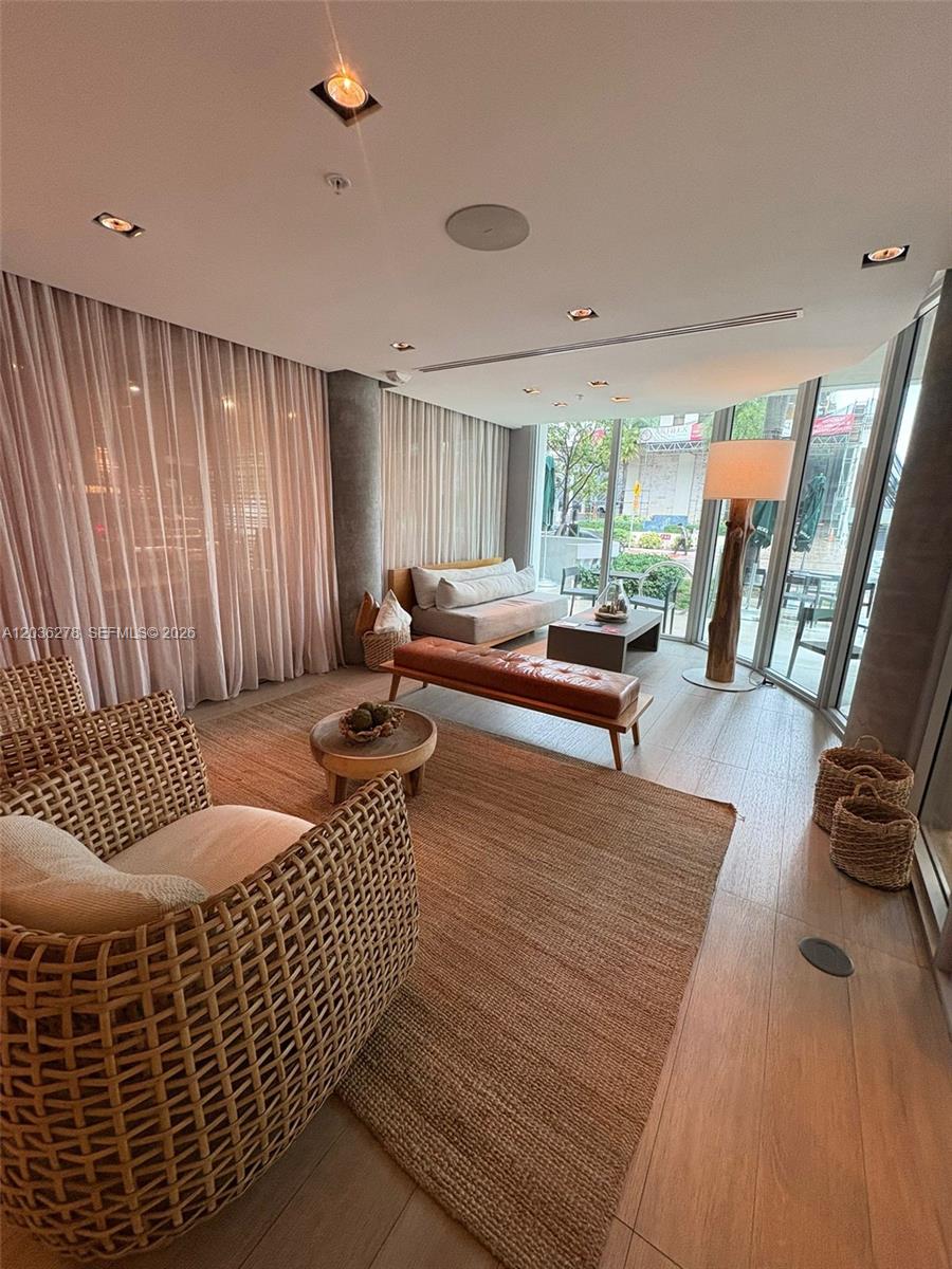 A modern living room features a woven armchair, leather bench, and floor-to-ceiling windows — 6080 Collins Ave # 506, Miami Beach FL 33140, MIAMI BEACH, FL