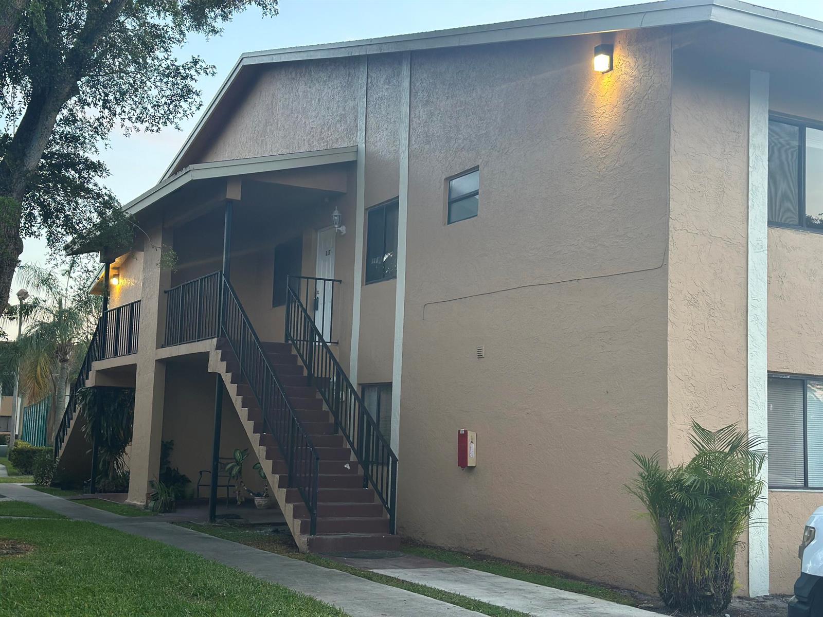 An exterior view of a two-story apartment building with an outdoor staircase and tan stucco — 6031 N 10th Ave Avenue N # 219, FL 33463, FL