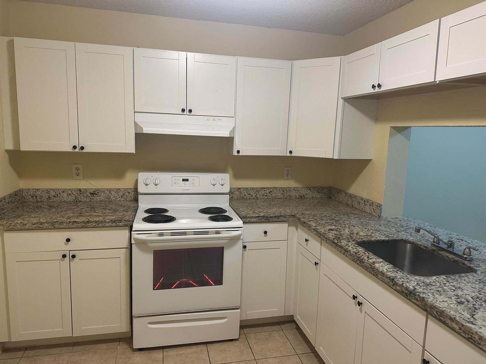 A kitchen features white cabinets, granite countertops, a white electric stove, and a stainless steel sink — 6031 N 10th Ave Avenue N # 219, FL 33463, FL