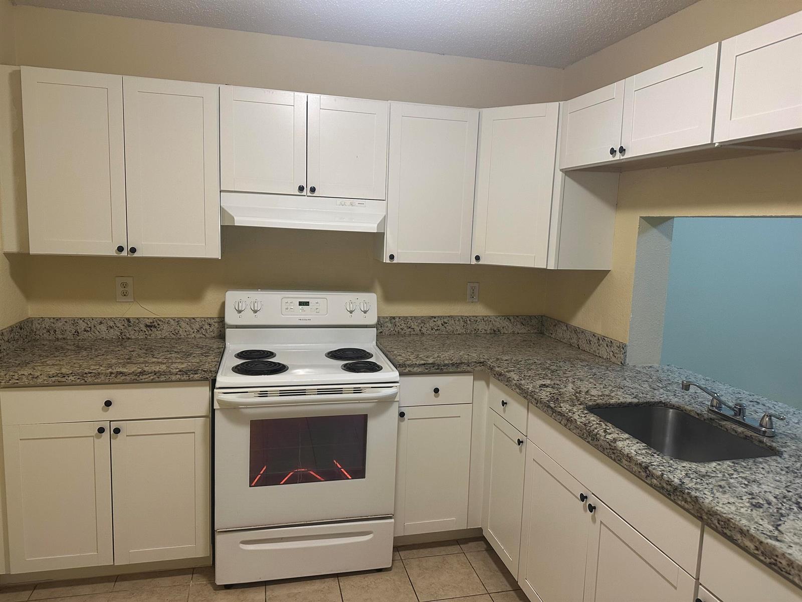 A kitchen features white cabinets, granite countertops, and a white electric range — 6031 N 10th Ave Avenue N # 219, FL 33463, FL