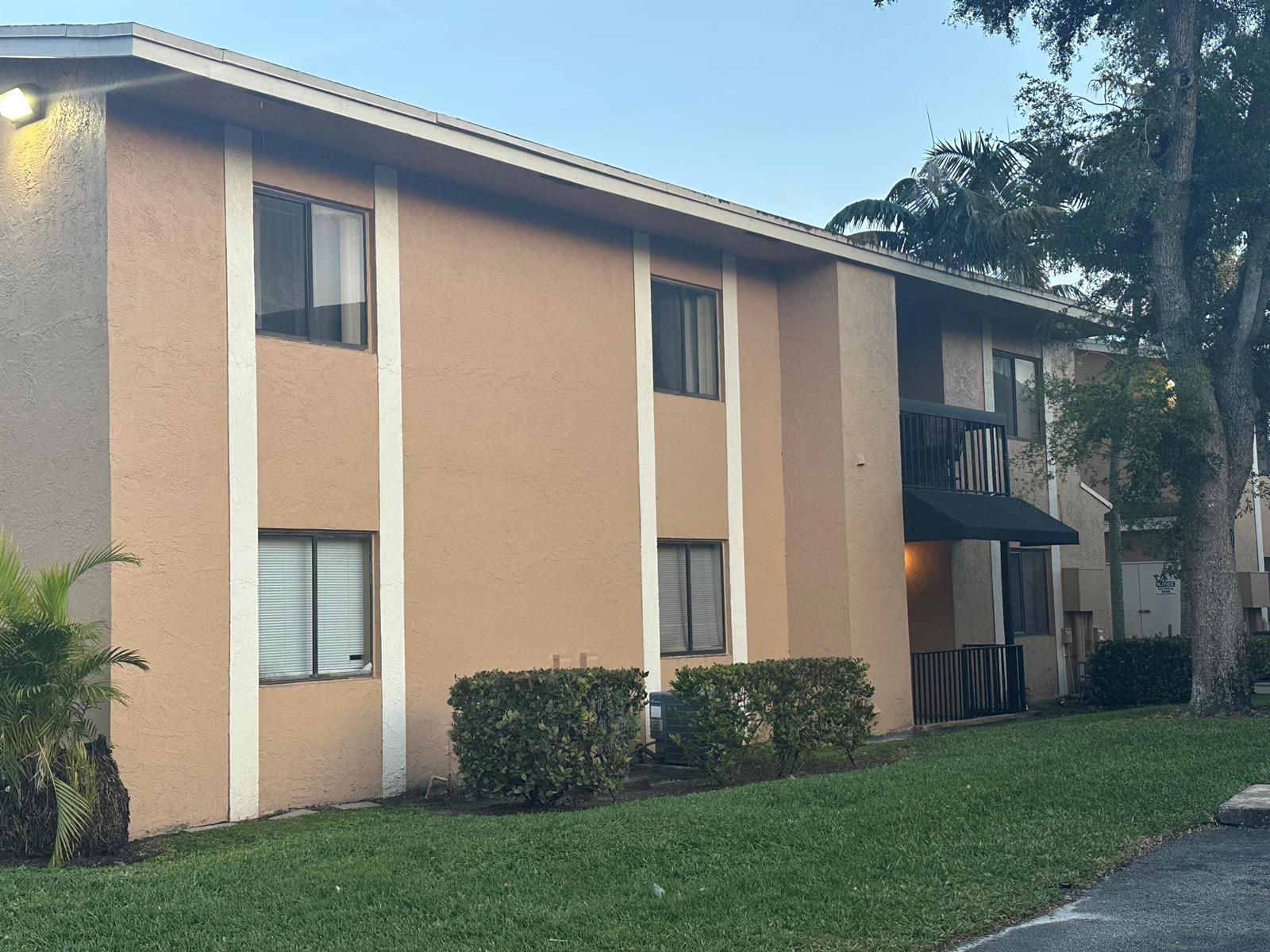 A two-story apartment building with tan stucco walls, white vertical accents, and a black balcony — 6031 N 10th Ave Avenue N # 219, FL 33463, FL