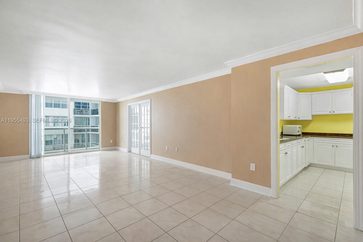 An empty living area with tile floors leads to a kitchen with white cabinets — 6039 Collins Ave # 1206, Miami Beach FL 33140, MIAMI BEACH, FL