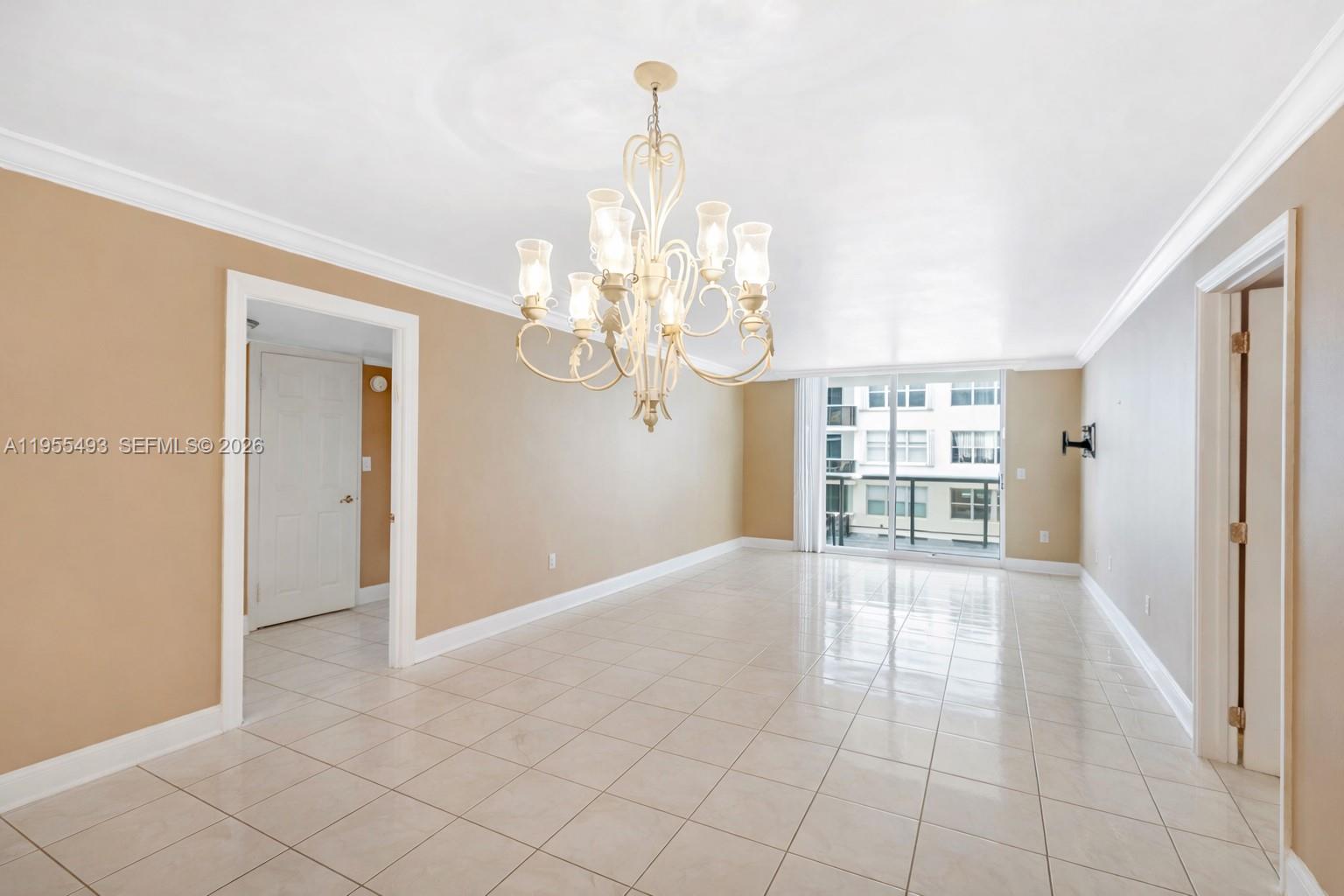 An empty room with beige walls, tile flooring, a chandelier, and a sliding glass door — 6039 Collins Ave # 1206, Miami Beach FL 33140, MIAMI BEACH, FL