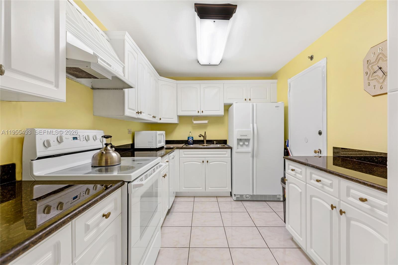 A kitchen features white cabinetry, dark countertops, a white stove, and a white refrigerator — 6039 Collins Ave # 1206, Miami Beach FL 33140, MIAMI BEACH, FL