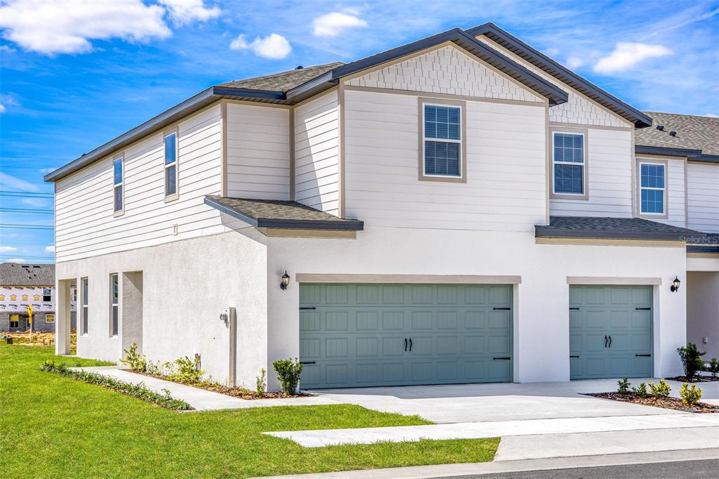 A two-story townhouse exterior features white siding, stucco walls, and two sage green garage doors — 678 POPPY LANE, DUNDEE, FL