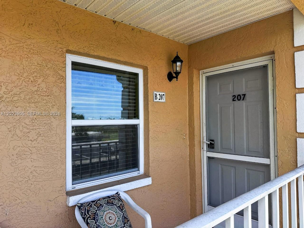 An exterior view shows a tan wall with a window, a door labeled 207, and a light fixture — NAPLES, FL
