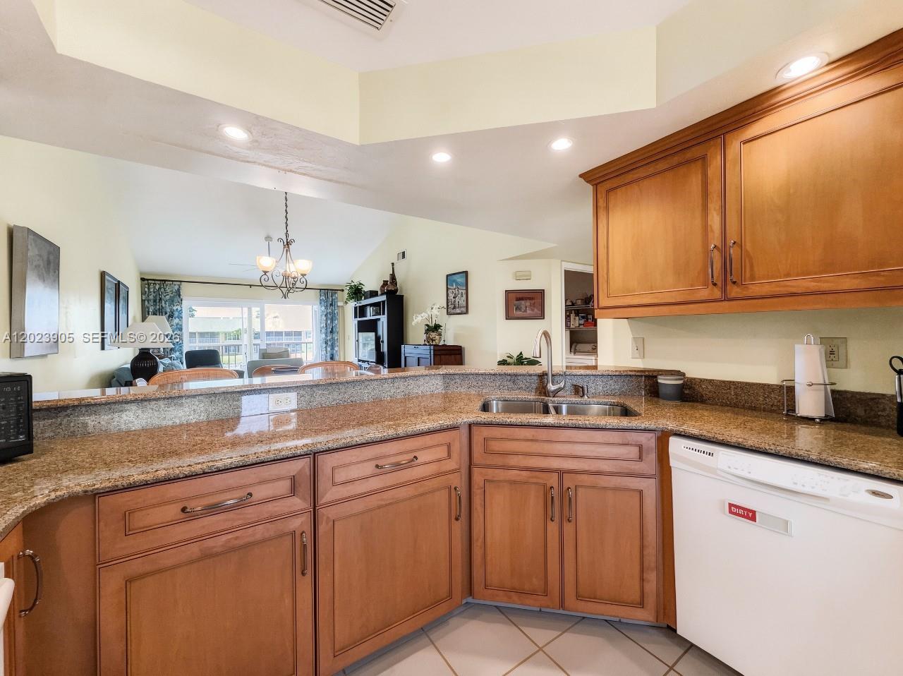 A kitchen features wood cabinets, granite countertops, a double sink, and a white dishwasher — NAPLES, FL