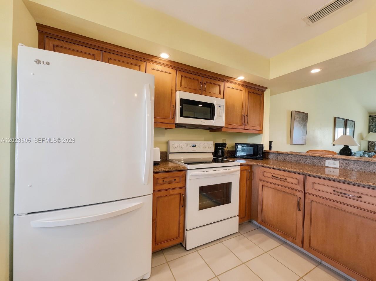 A kitchen features wood cabinets, granite countertops, and white appliances — NAPLES, FL