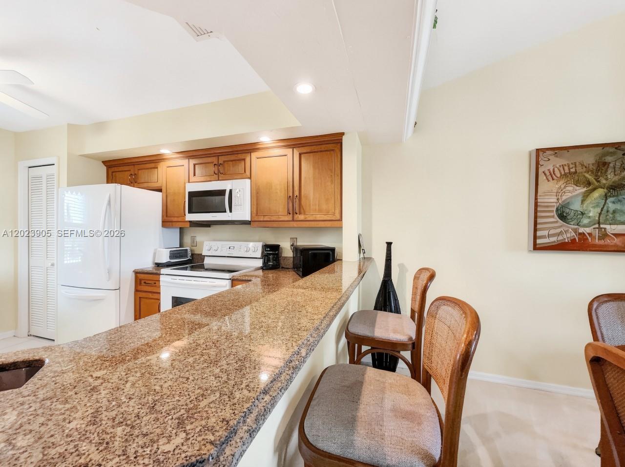 A kitchen features wood cabinets, granite countertops, a white refrigerator, and a breakfast bar — NAPLES, FL