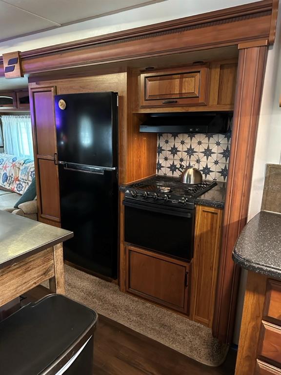 A kitchen in a recreational vehicle features a black refrigerator, stove, and patterned backsplash — 25208 NE 143RD STREET, SALT SPRINGS, FL