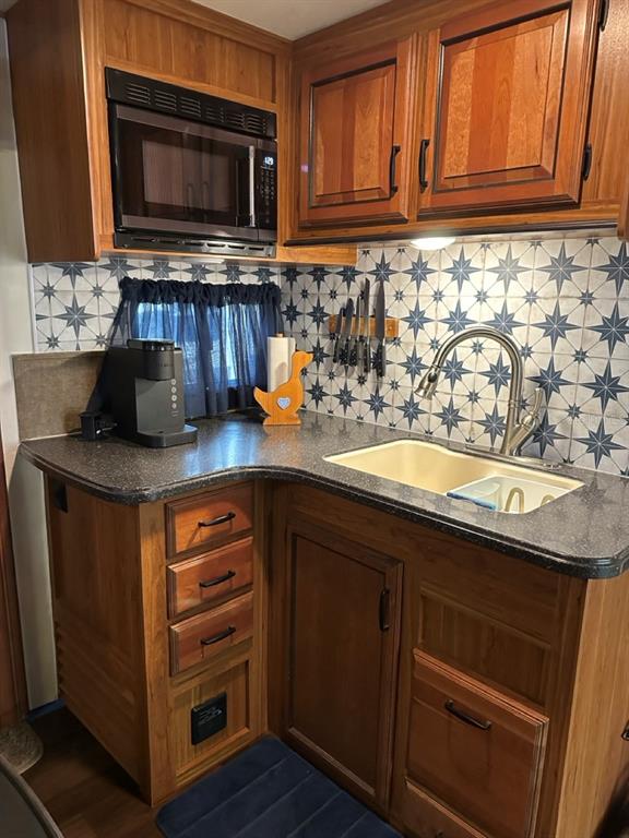 A kitchen features wood cabinets, a dark countertop, a patterned backsplash, and a double sink — 25208 NE 143RD STREET, SALT SPRINGS, FL