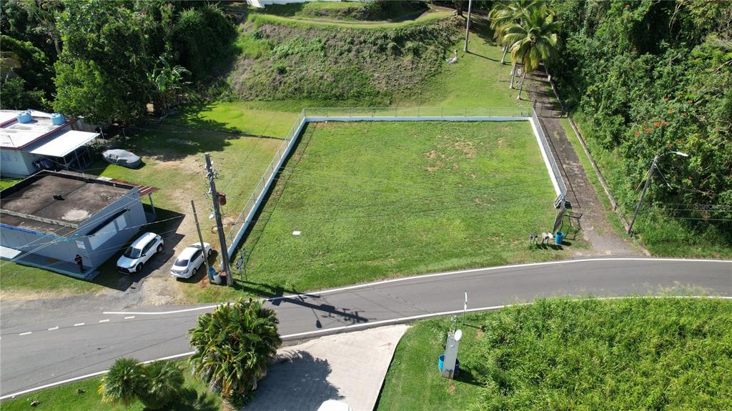 An aerial view shows a fenced, rectangular grassy lot situated next to a paved road — 637ST BO MIRAFLORES #8-A, ARECIBO, PR