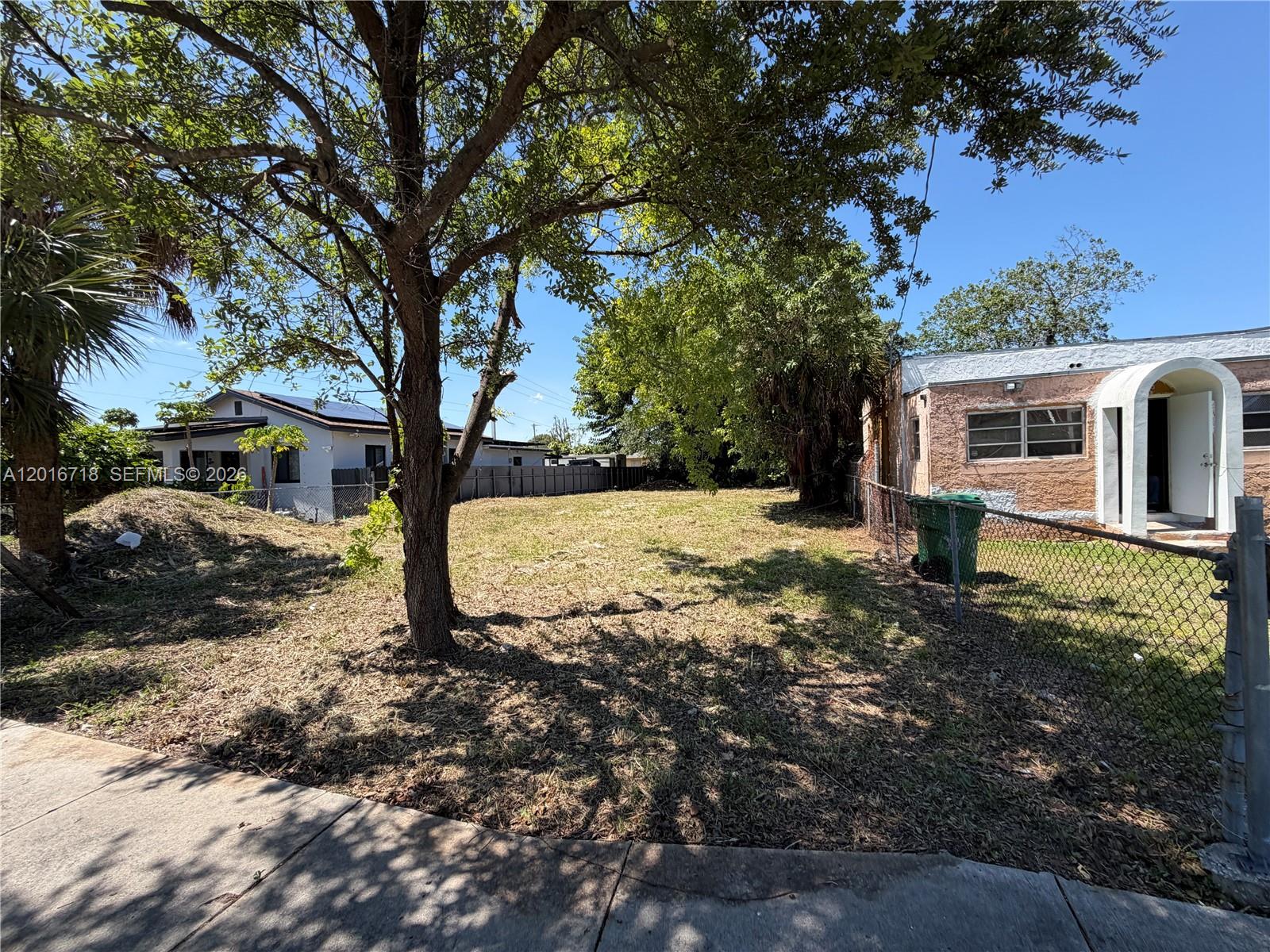 A grassy vacant lot sits between two residential houses under a clear blue sky — 2381 NW 63rd st, Miami FL 33147, MIAMI, FL