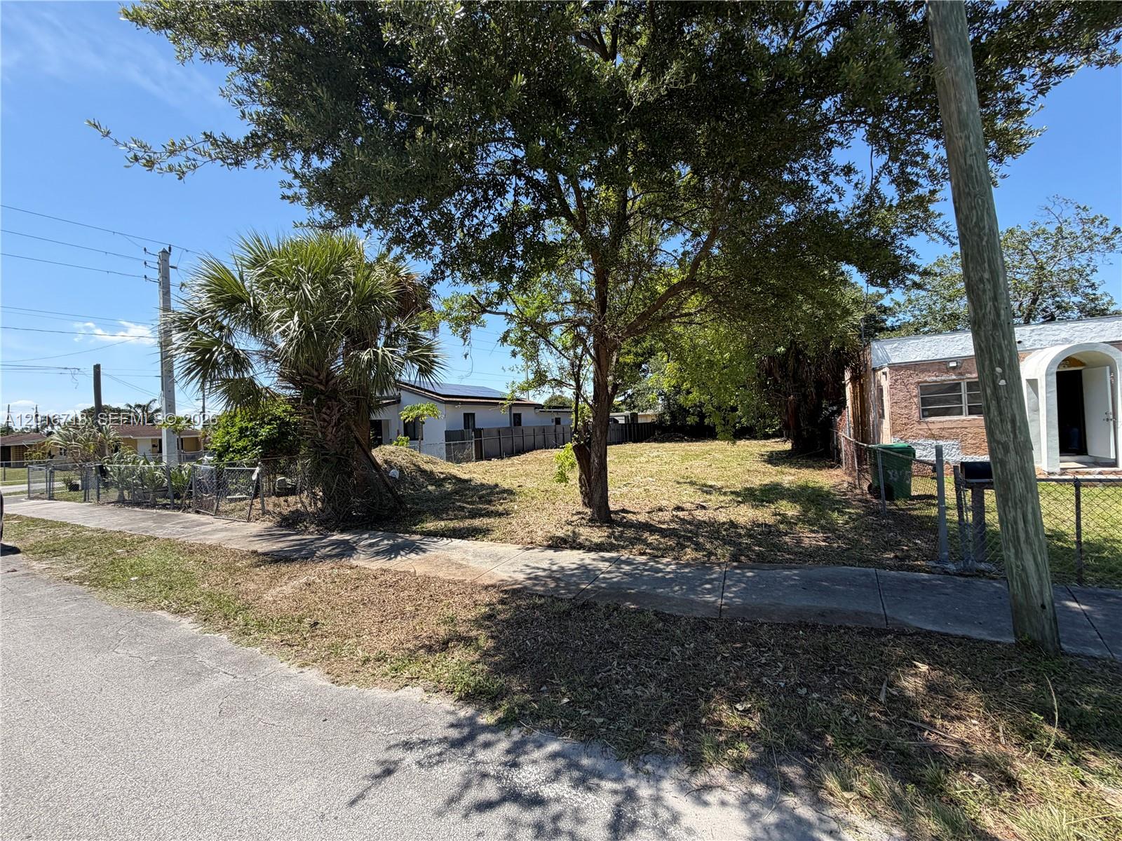 A vacant residential lot sits between two houses with a sidewalk and trees in front — 2381 NW 63rd st, Miami FL 33147, MIAMI, FL