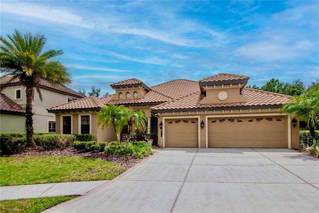 A single-story house with a tile roof, three-car garage, and palm trees in the front yard — 20110 POND SPRING WAY, TAMPA, FL