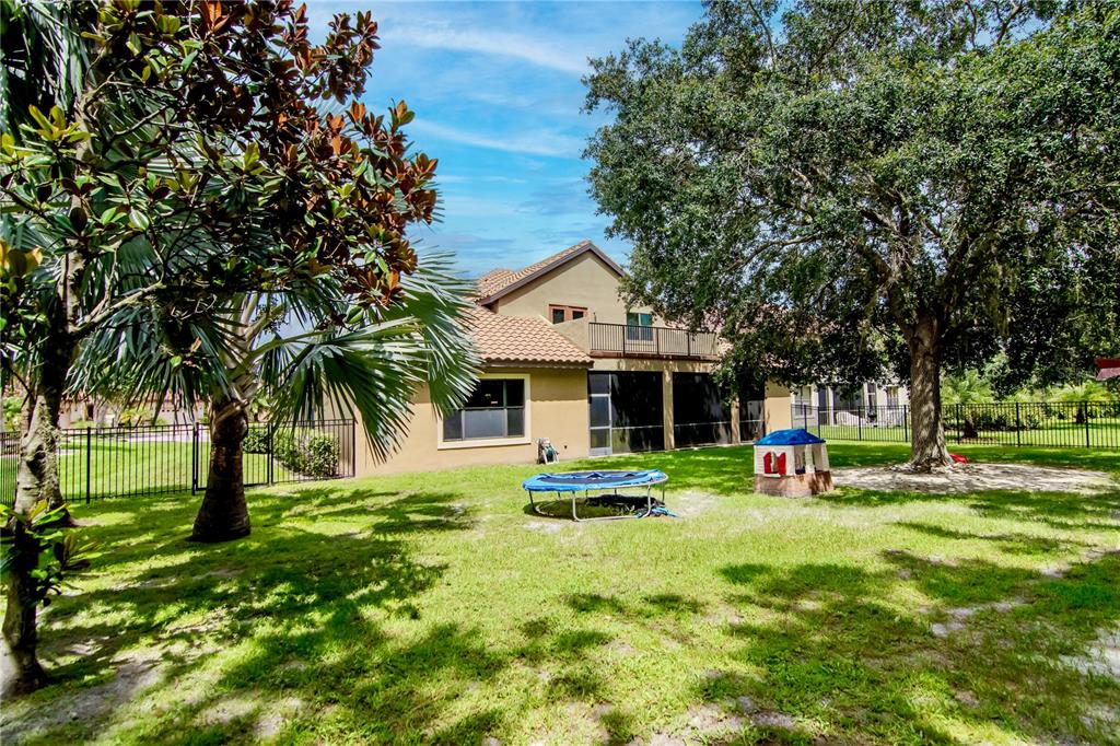 A backyard features a tan house with a screened patio, a trampoline, and large trees — 20110 POND SPRING WAY, TAMPA, FL