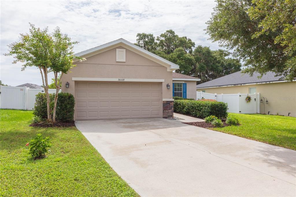 A single-story suburban house with a beige stucco exterior, a two-car garage, and a driveway — 36108 LAGUNA HILLS CIRCLE, ZEPHYRHILLS, FL