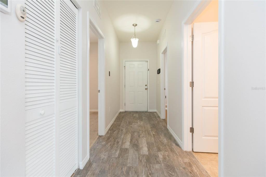 A hallway with wood-look flooring, white walls, and a white front door at the end — 36108 LAGUNA HILLS CIRCLE, ZEPHYRHILLS, FL