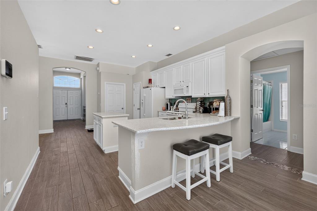 A white kitchen with an island, granite countertops, and wood-look tile flooring — 264 LAUREL RIDGE PASS, DAVENPORT, FL